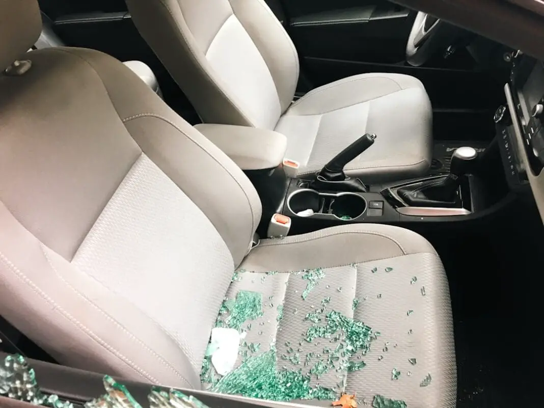 the aftermath of a car break-in, with shattered glass scattered across the passenger seat. The side window has been broken during a theft.