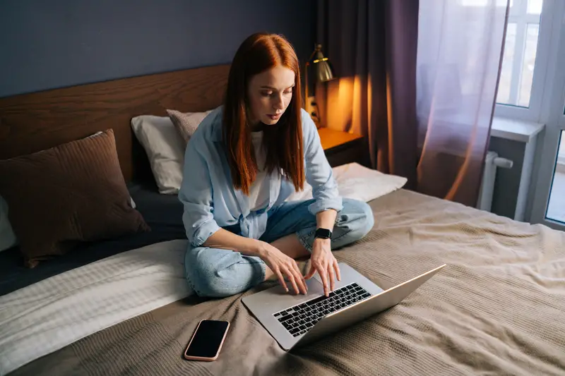 High-angle shot of young woman looking on laptop screen sitting in bed at cozy bedroom