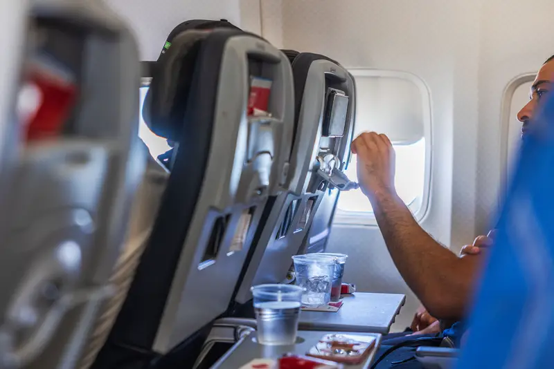 View of passenger watching smartphone attached to airplane seat with cola and biscuits on table during American Airlines flight.
