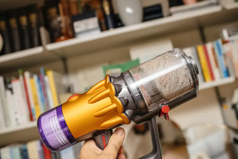 POV male hand holding new cordless vacuum cleaner by Dyson V12 with filled bin