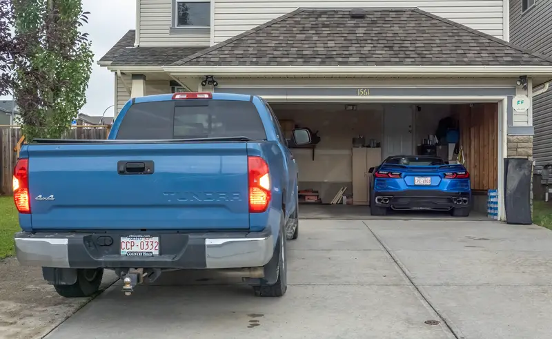 Blue Toyota Tundra in driveway with a blue sports car visible inside an open garage at a