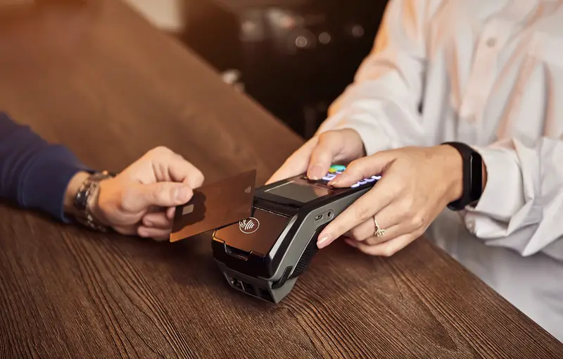 The customer`s hand pays for a contactless credit card with NFC technology. Bartender with a Credit Card reader. Focus on hands