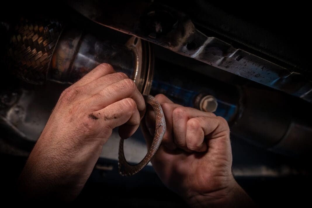 Close-up of a mechanic's grease-stained hands using a wrench beneath a car during an engine repair in a workshop.